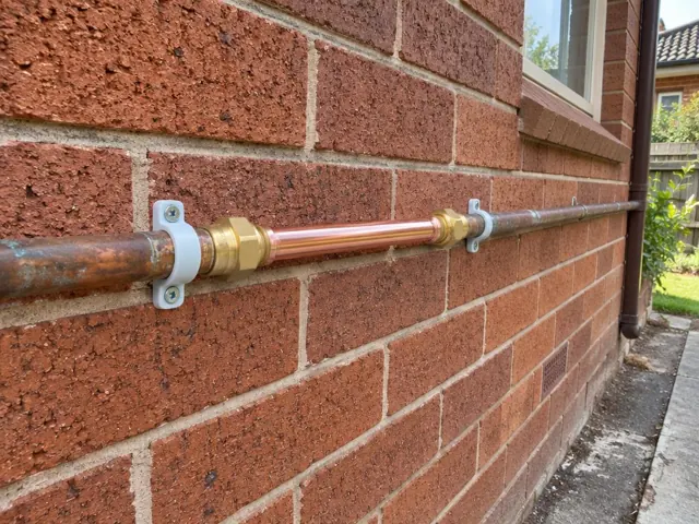 Repaired copper water pipe section on a brick exterior wall beside a window in Kings Park